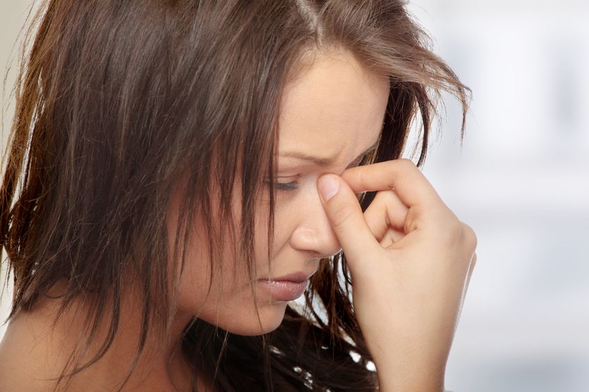woman holding the bridge of her nose in pain from a headache